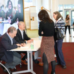 Gov. Baker and Steve Kadish sit at a table signing copies of their book for two event attendees
