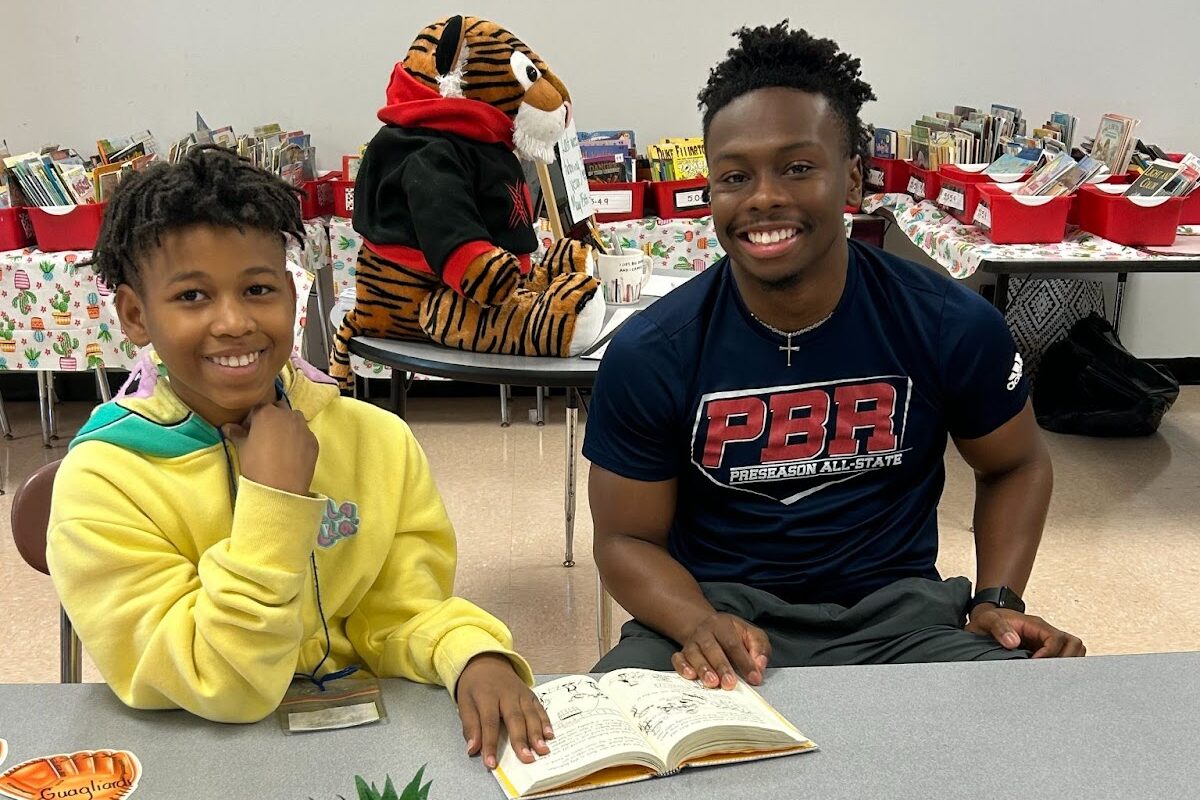 An elementary school student reads a book alongside a high school student.