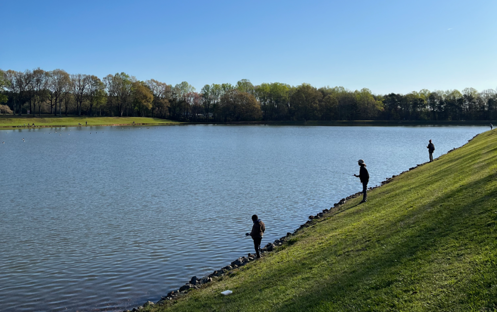 Three people fish from the bank of a large lake