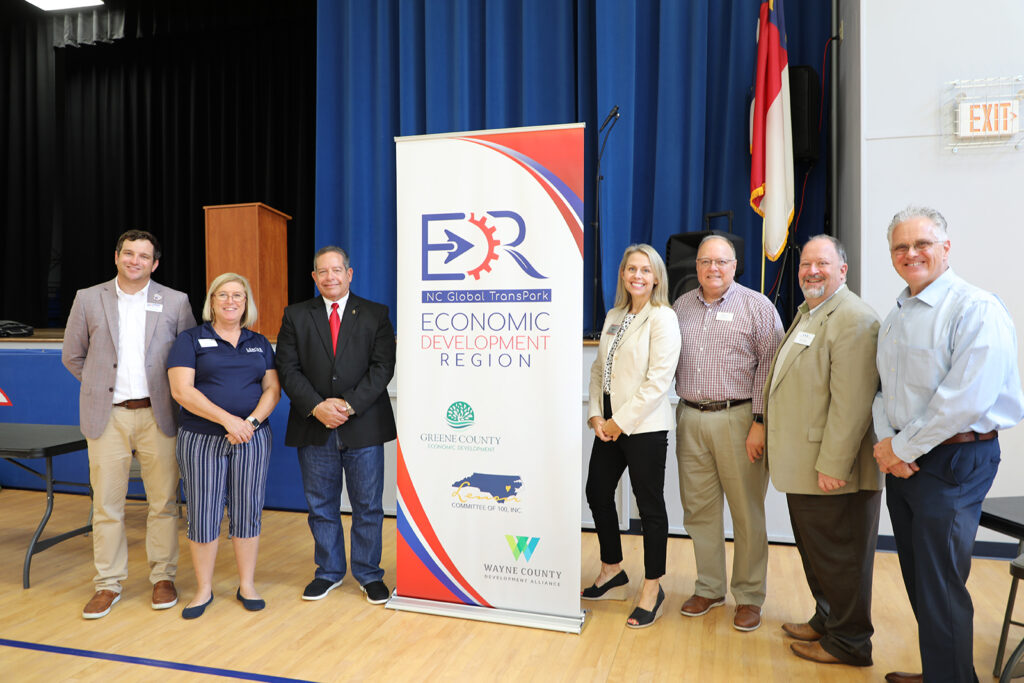 Seven people stand posing by a banner for the Economic Development Region.