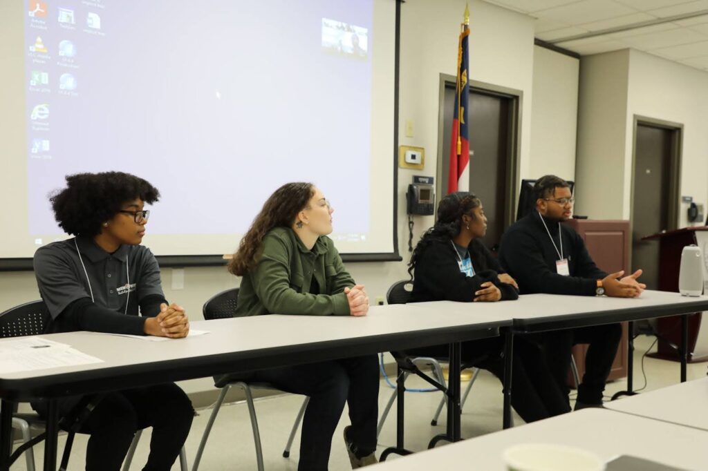 Four young people sit on a panel at the front of a room