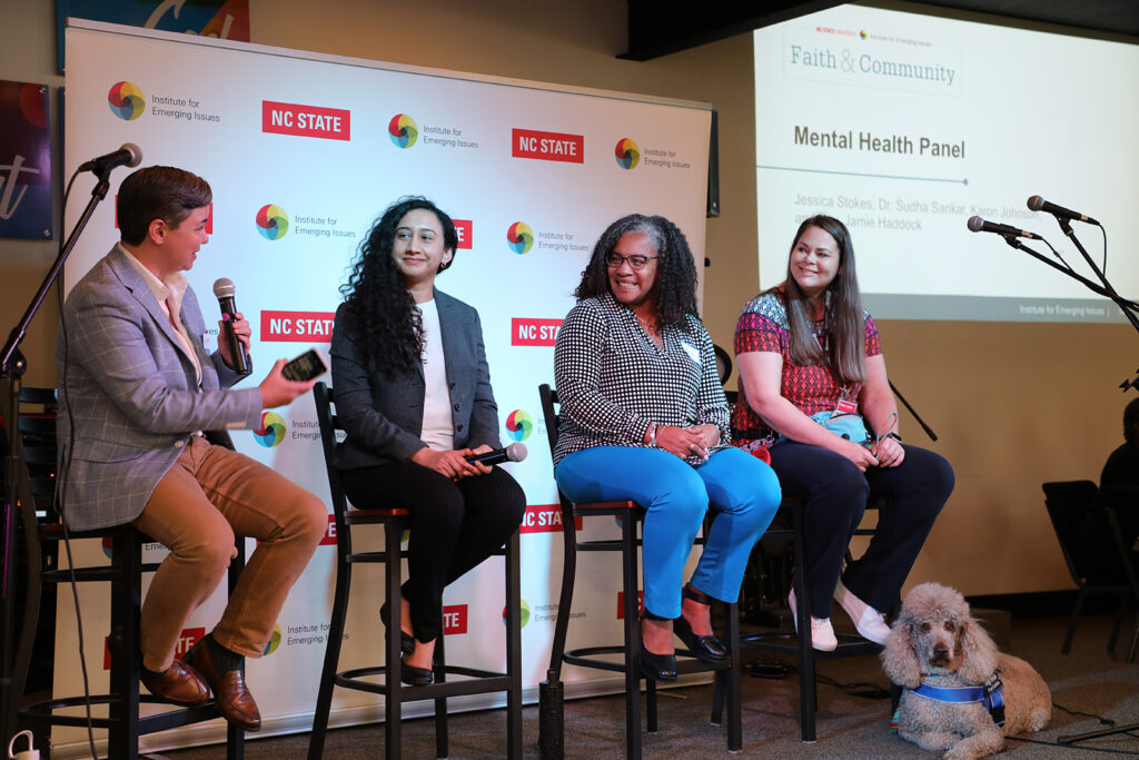 Four speakers sit on tall stools at the front of a room as part of a panel discussion on mental health