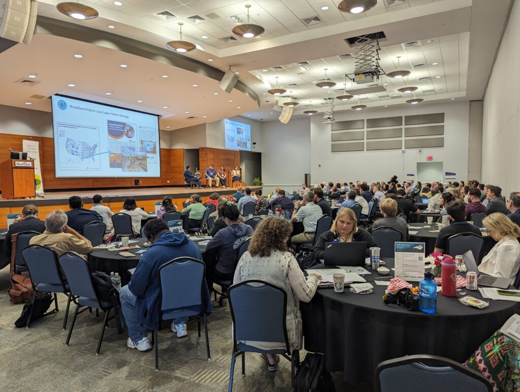 A group of more than 100 people sit at tables, attending a day-long conference