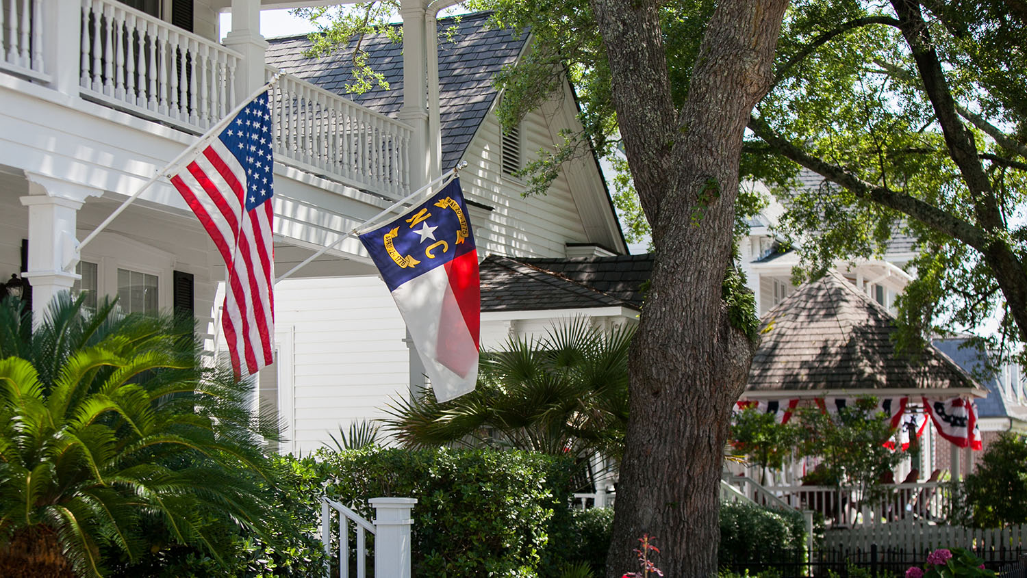 Front of a white house with a North Carolina flag and United States flag flying on the front porch